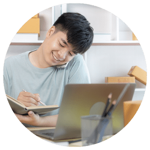 person writing in a notebook in front of a computer